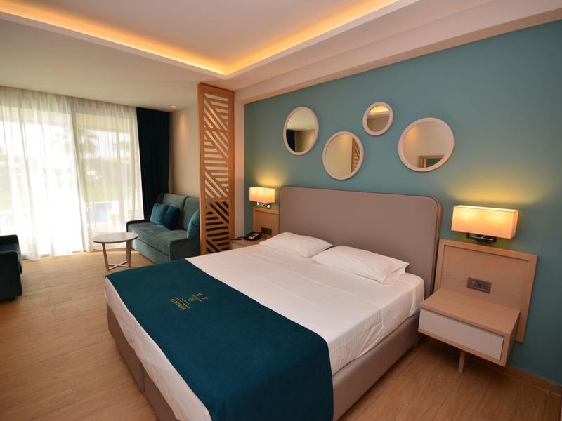 Moderne hotelkamer met tweepersoonsbed, blauwe accentmuur, ronde spiegels en zachte verlichting.