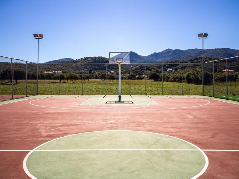 Buitenspeelveld voor basketbal met uitzicht op bergen onder een heldere blauwe lucht.