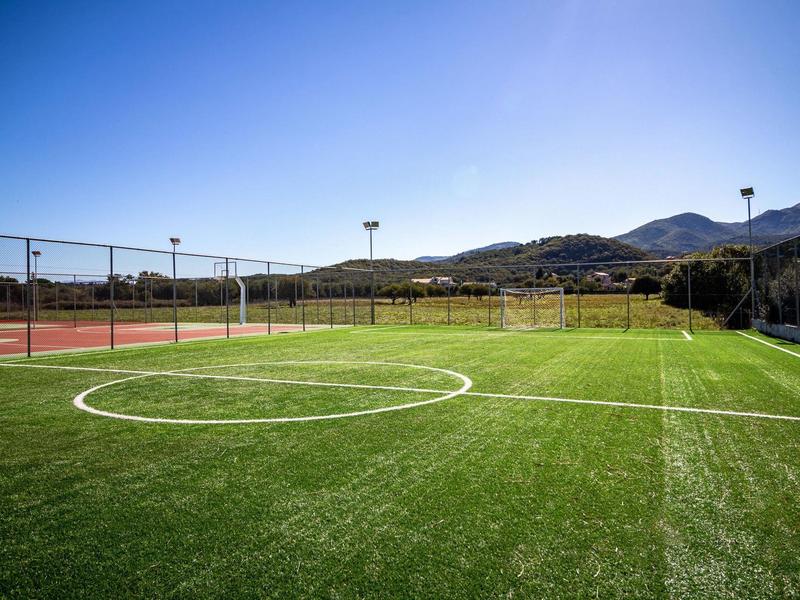 Buiten sportveld met kunstgras en heldere blauwe lucht, omringd door heuvels.