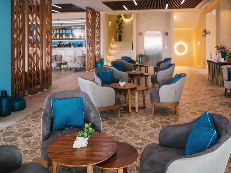 Moderne hotel lobby met comfortabele fauteuils, blauwe kussens, houten tafels en decoratieve schermen.