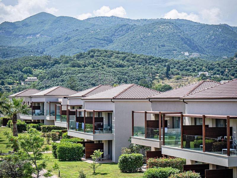 Moderne hotelgebouwen met balkons omgeven door groene gazons en bergzicht.