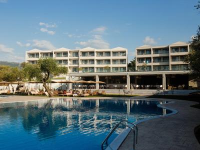 Modern hotel met groot buitenzwembad, ligstoelen en helderblauwe lucht.