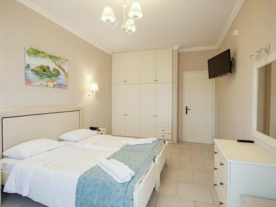 Helles Schlafzimmer mit Doppelbett, weißen Möbeln, Wandschrank, Spiegel und Wandfernseher.