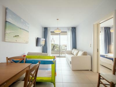 Moderner Wohnraum mit Essbereich, Sofa, Babyreisebett und Zugang zum Balkon mit Meerblick.