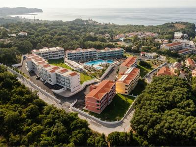 Luftaufnahme einer Wohnanlage mit roten Dächern, viel Grün und Blick auf das Meer im Hintergrund.