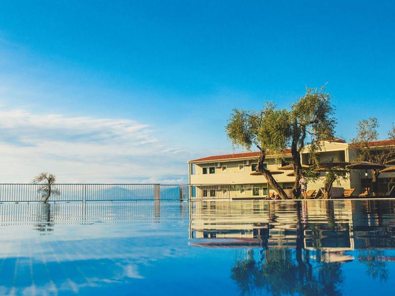 Ruhiger Pool mit klarer Spiegelung von Bäumen und Gebäude unter blauem Himmel am Wasser.