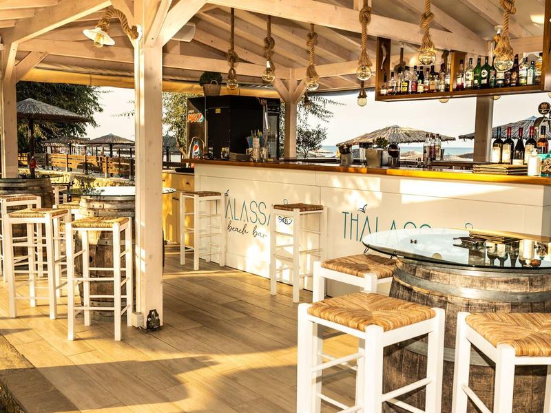 Heller Außenbereich mit Holzstühlen, Bartresen und Dachkonstruktion aus Holz an sonnigem Tag.