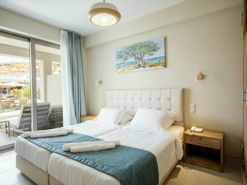 Helles Schlafzimmer mit Doppelbett, blauer Decke, Nachttisch, Schrank und Zugang zur Terrasse.