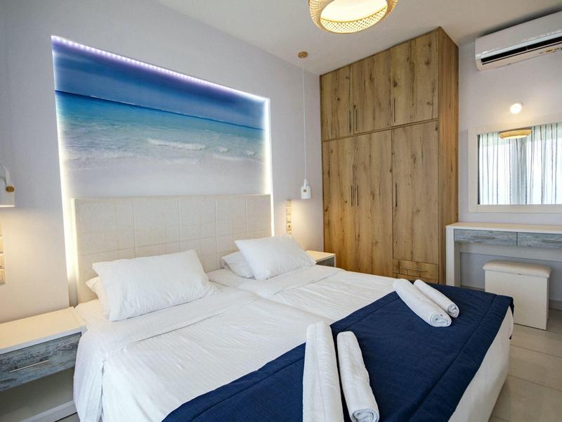 Hell eingerichtetes Schlafzimmer mit zwei Einzelbetten, blauer Bettdecke und großem Strandbild über dem Bett.