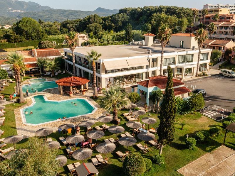 Hotel mit Außenpool, Liegestühlen und Sonnenschirmen, umgeben von Bäumen und Bergen.