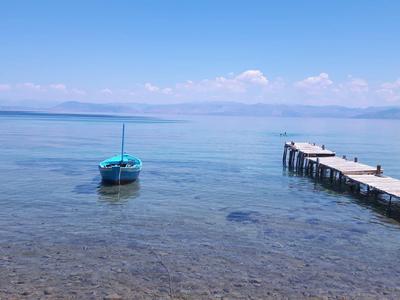 Blaues Boot nahe einem langen Steg auf klarem ruhigem Meerwasser unter blauem Himmel