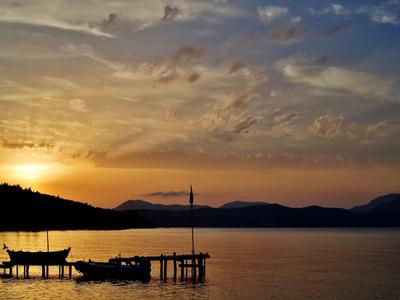Coucher de soleil sur un lac calme avec une jetée et un petit bateau.