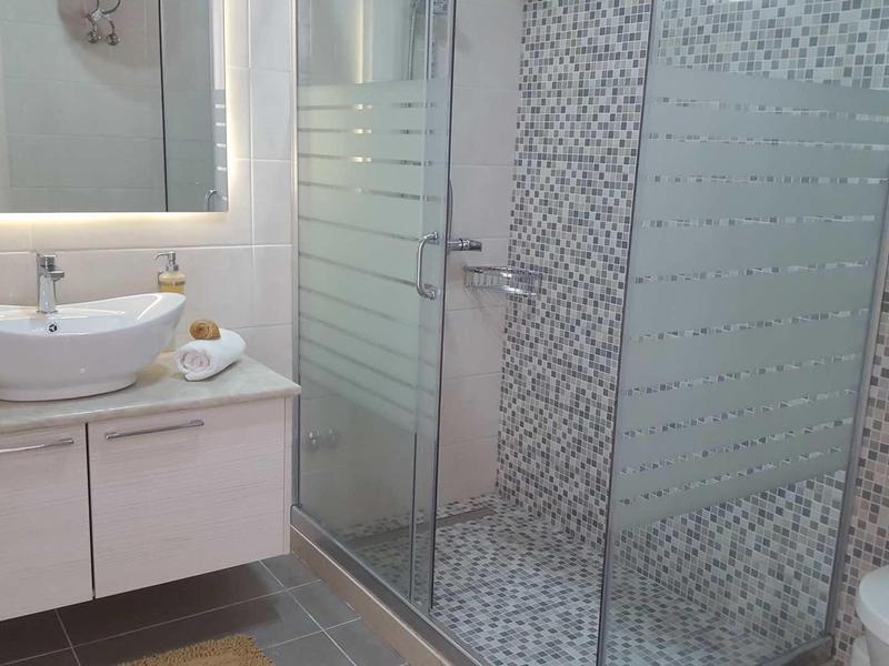 Salle de bain moderne avec lavabo, armoire intégrée et douche à porte vitrée avec carreaux mosaïques.