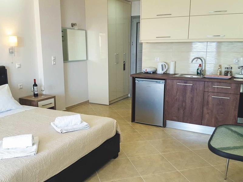 Chambre d'hôtel lumineuse avec lit double, kitchenette et sol carrelé.