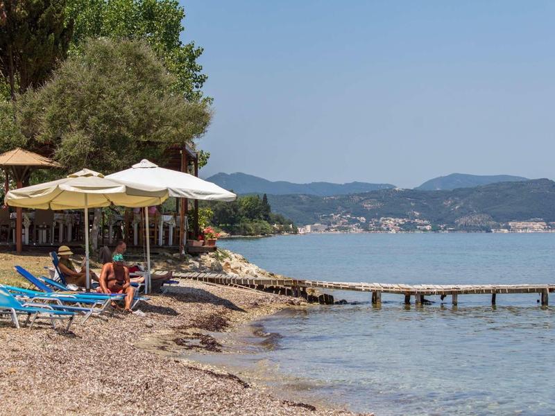 Plage avec chaises longues, parasols et jetée au bord de l'eau calme sous un ciel clair.