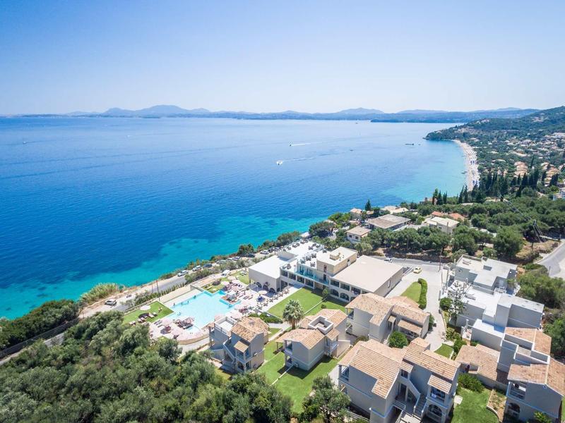 Luftaufnahme eines Küstenorts mit blauem Meer, Stränden, Hotels und grüner Vegetation.