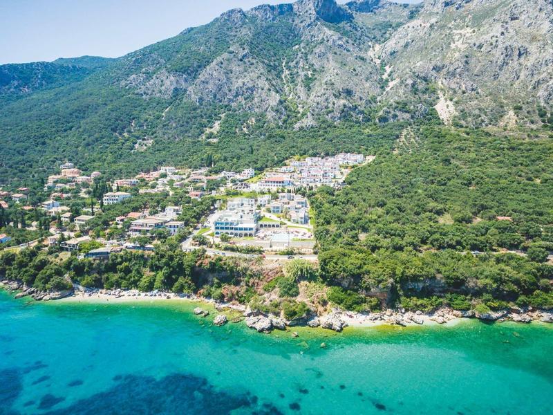 Küstenlandschaft mit klarem türkisfarbenem Wasser, grün bewaldeten Hügeln und kleinen Gebäuden.