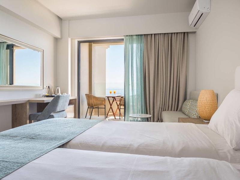 Helles Hotelzimmer mit zwei Betten, Schreibtisch, großem Spiegel und Balkon mit Tisch und Stühlen.