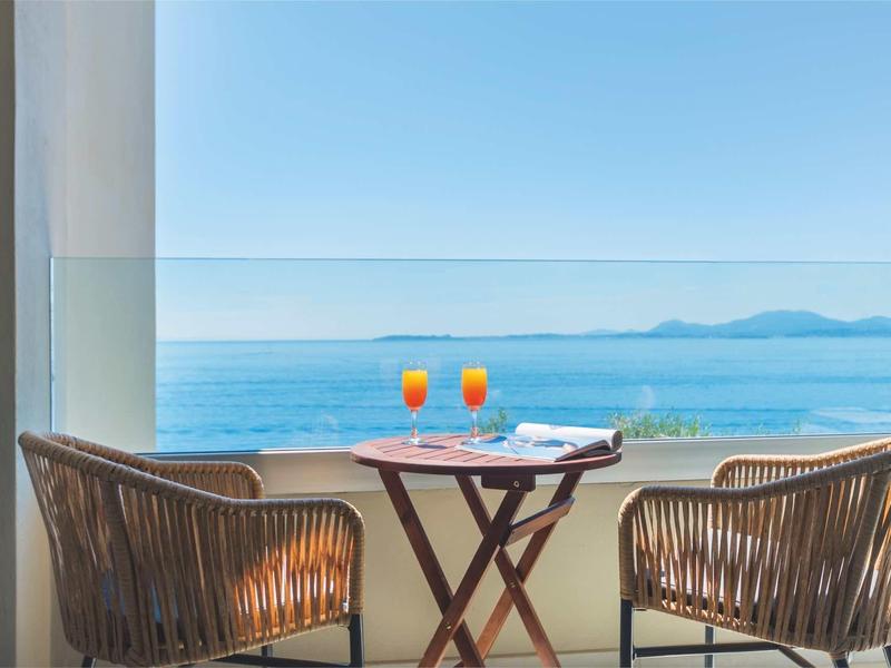 Terrassenblick aufs Meer mit zwei Stühlen, Tisch und zwei Orangensaftgläsern bei klarem Himmel.