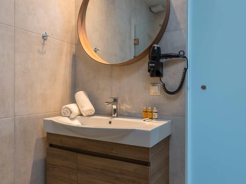 Moderner Waschtisch mit Holzschrank, rundem Spiegel, Handtüchern und Haartrockner an grauer Wand.