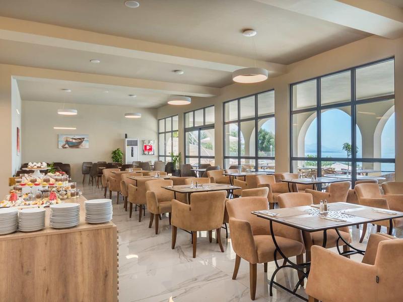 Großer heller Speisesaal mit vielen Tischen, braunen Stühlen und großen Fenstern mit Blick nach draußen.