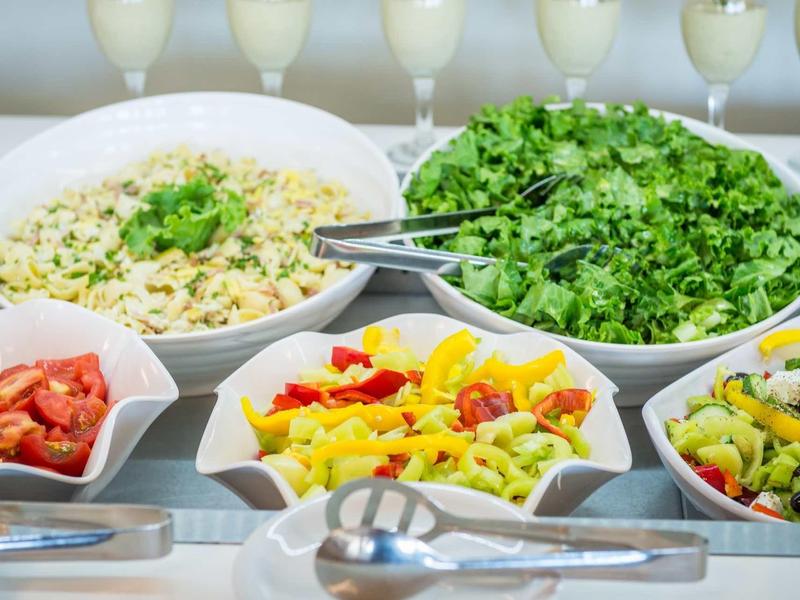 Verschiedene frische Salate in weißem Geschirr, mit grünen, bunten und roten Zutaten, serviert mit Besteck.