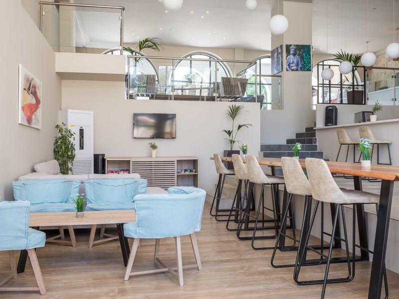 Moderner Wohnraum mit blauen Sesseln, Holztisch, Barhockern und hellen Wänden.