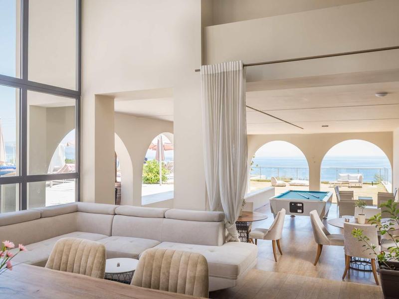 Helles Wohnzimmer mit großen Fenstern, weißem Sofa, Esstisch, Billiardtisch und Meerblick.