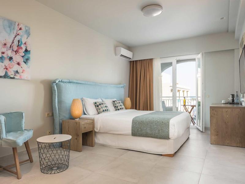 Modernes Schlafzimmer mit großem Bett, blauem Sessel, Balkon und neutralen Farben.