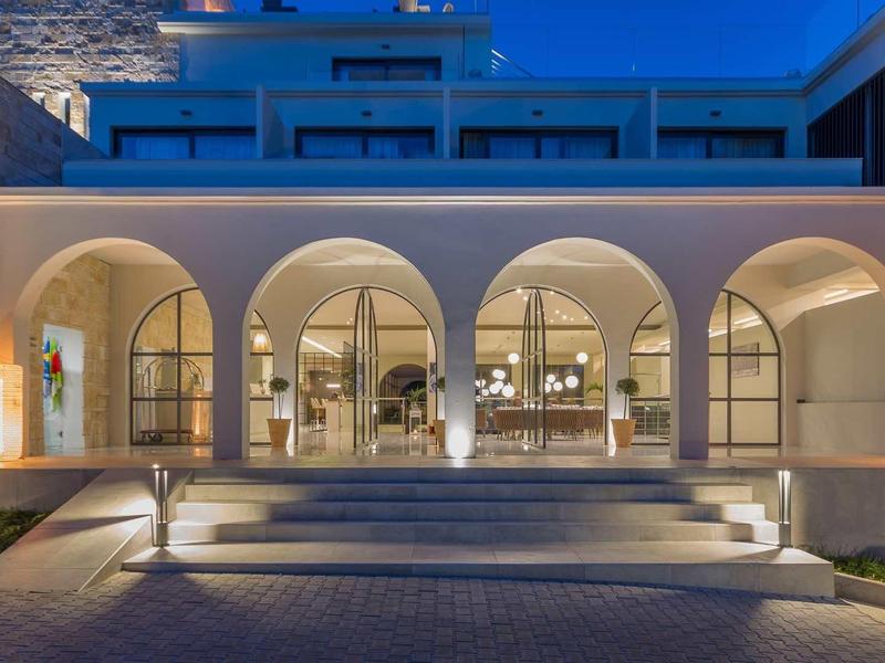 Beleuchtete Terrasse mit Bögen und Treppen vor modernem Gebäude in Abenddämmerung.