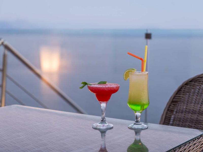 Zwei bunte Cocktails stehen auf einem Tisch am Wasser mit Weitblick und Stuhl aus Geflecht.