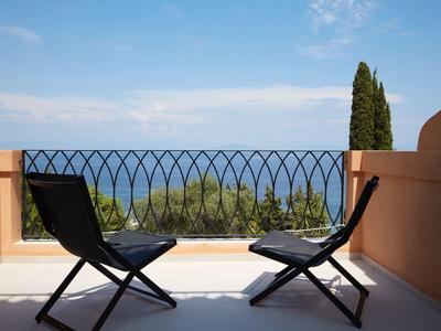 Dwa czarne składane krzesła na balkonie z widokiem na morze i drzewa.