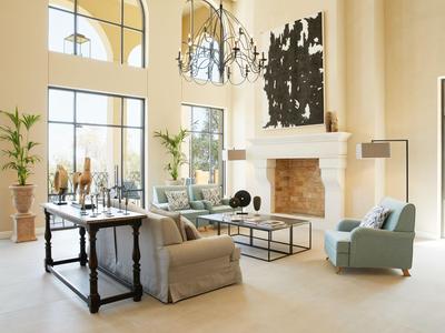 Soggiorno luminoso con finestre alte, camino, poltrone comode e arredamento moderno.