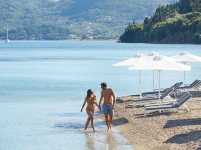 Coppia che si tiene per mano camminando sulla spiaggia vicino a sdraio e ombrelloni.