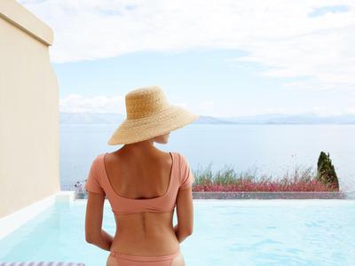 Donna con cappello di paglia guarda una piscina con vista sul mare e sul cielo.