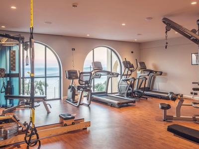 Palestra luminosa con pavimenti in legno e attrezzature moderne davanti a grandi finestre ad arco.