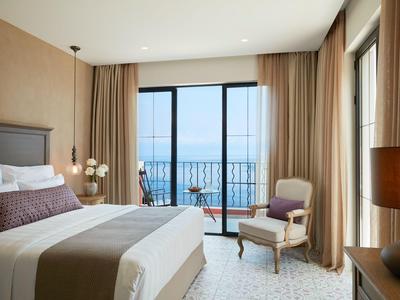 Camera d'hotel moderna con letto grande, poltrona e balcone con vista sul mare.