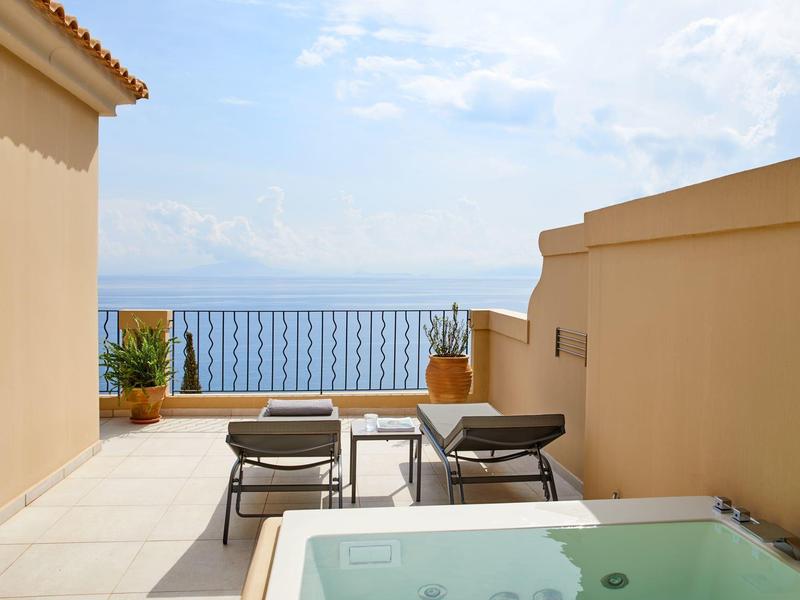 Taras z jacuzzi, leżakami i widokiem na morze w słoneczny dzień.