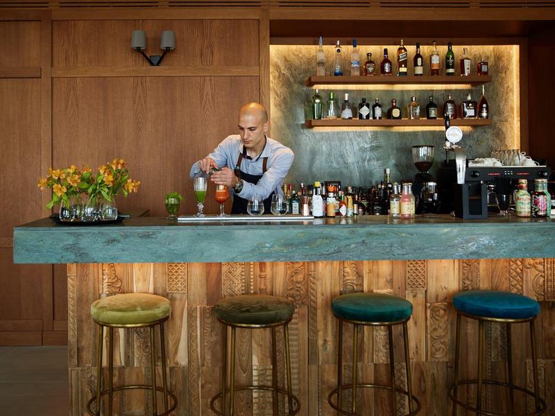 Barman przygotowujący drinki przy nowoczesnym barze z zielonym blatem i stołkami.