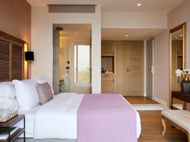 Nowoczesny pokój hotelowy z łóżkiem podwójnym, fioletową narzutą, drewnianymi meblami i przyległą łazienką.