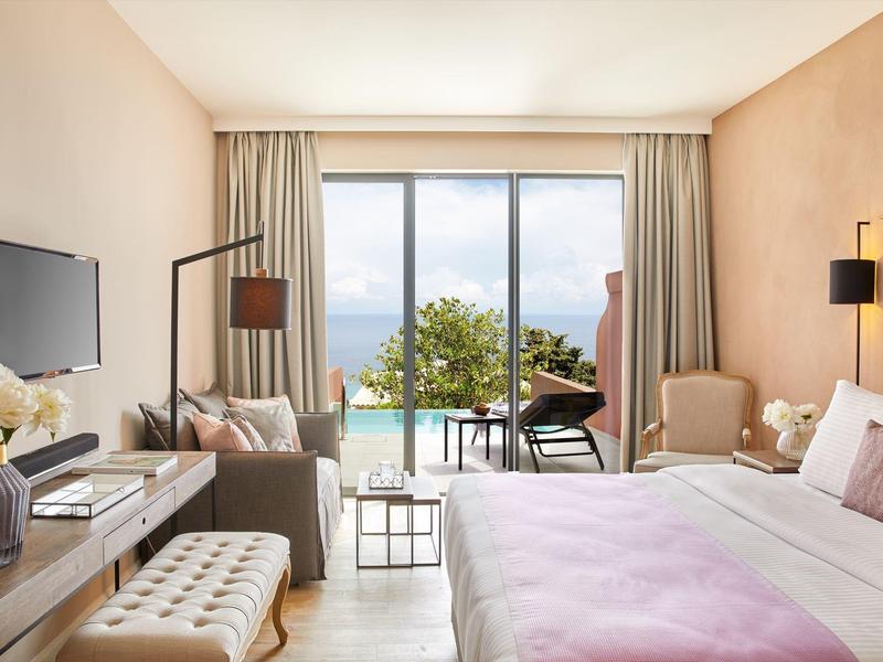 Przytulny pokój hotelowy z dużym łóżkiem, przestrzenią wypoczynkową i widokiem na morze przez panoramiczne okno.