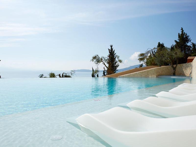 Basen infinity z białymi leżakami z widokiem na morze pod niebieskim niebem.