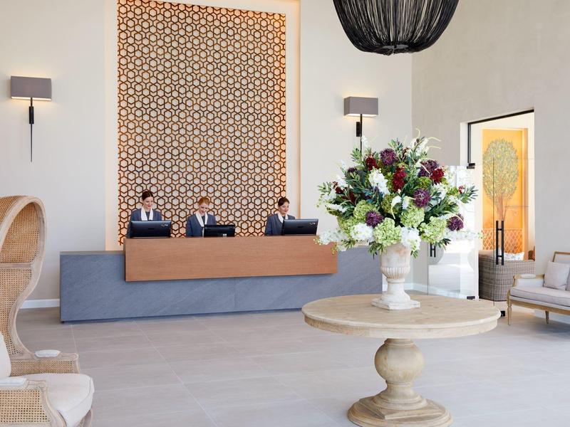 Hol hotelowy z recepcją, trzema pracownikami i elegancką dekoracją kwiatową na okrągłym stole.