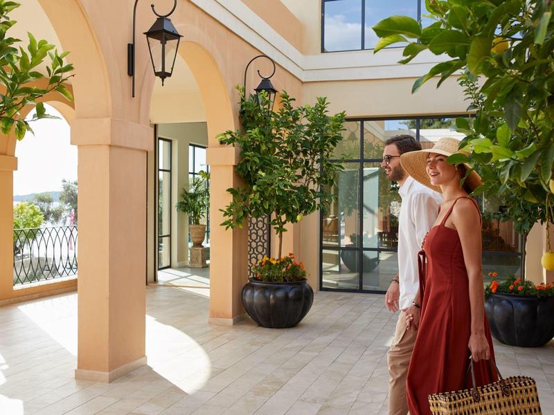 Para spacerująca przez słoneczne dziedzińce hotelu z drzewami pomarańczowymi.