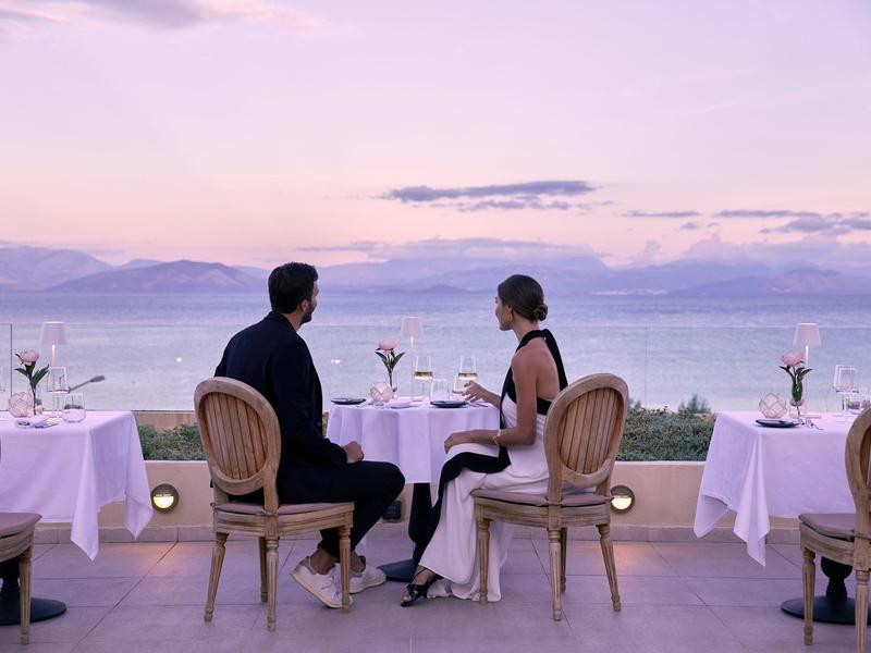 Para siedzi w eleganckiej restauracji z widokiem na morze i zachód słońca.