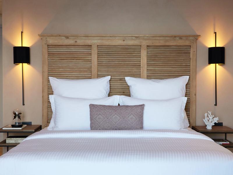 Nowoczesny pokój hotelowy z dużym białym łóżkiem, drewnianym zagłówkiem i lampami ściennymi