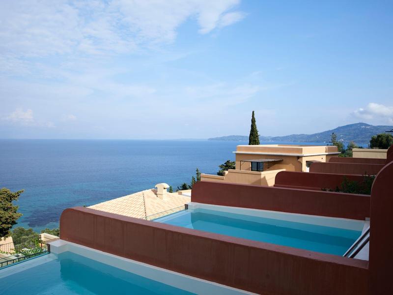 Basen hotelowy z widokiem na morze i jasne niebieskie niebo w tle.