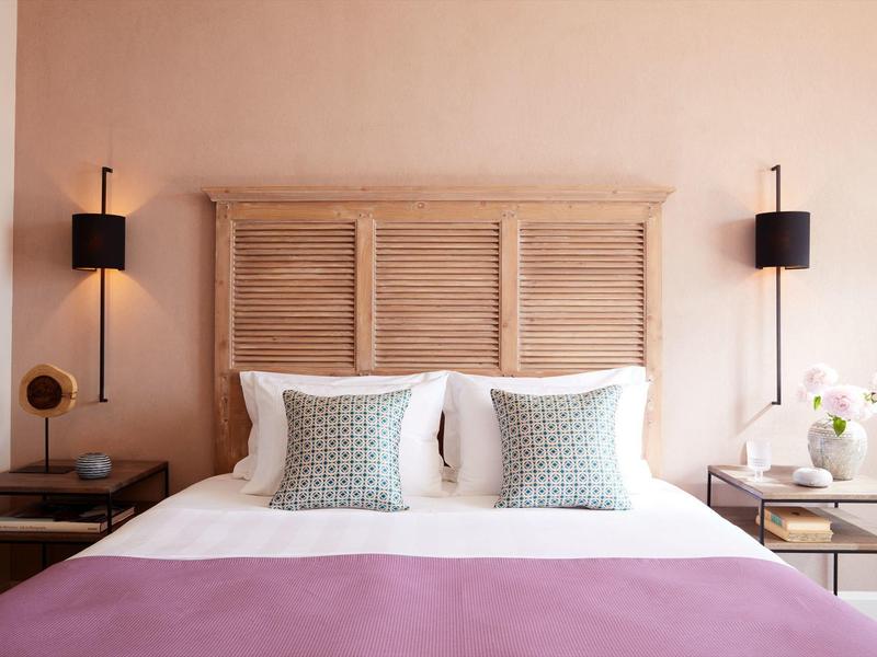 Przytulne podwójne łóżko z drewnianym zagłówkiem, białą pościelą, dwoma poduszkami i fioletowym kocem.