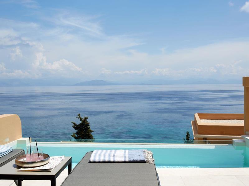 Basen typu infinity z leżakiem z widokiem na spokojne, niebieskie morze pod błękitnym niebem.