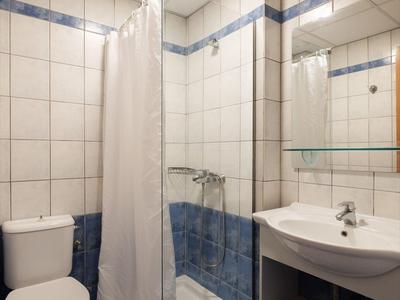 Compacte hotelbadkamer met wit- en blauwtiled muren, douche, toilet en wastafel met spiegel.